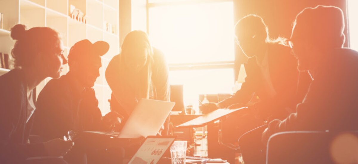 Silhouette of startup business team. Meeting on the couch. Big open space office. Five people. Intentional sun glare and lens flares. Wide screen, panoramic